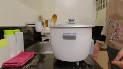 Asiatische-Hausfrau-Bewegt-Reiskocher-Und-öffnet-Den-Deckel-In-Der-Küche