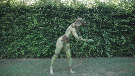 Wide-shot-of-a-female-model-wearing-green-bodypaint-dancing-slowly-in-nature,-in-the-style-of-nature-inspired-forms