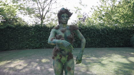 Wide-shot-of-a-female-model-wearing-green-bodypaint-walking-and-dancing-slowly-in-nature,-in-the-style-of-nature-inspired-forms