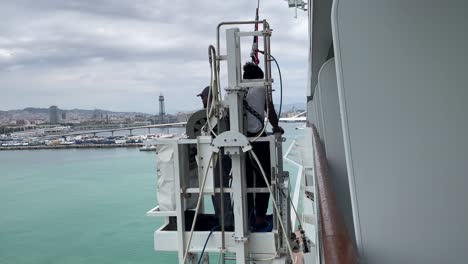 High-rise-window-washer-standing-on-window-washing-systems-cleaning-the-MSC-Grandiosa-cruise-ship-in-Port-of-Barcelona,-Spain