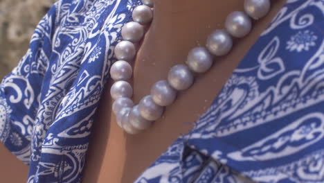 Cinematic-shot-of-a-statement-natural-pearl-necklace-on-a-womans-neck-wearing-a-blue-blouse-on-the-beach,-Slomo,-120-FPS