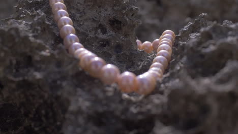Cinematic-shot-of-a-pearl-necklace-laying-on-marine-rock-on-a-beach,-120-FPS,-Slomo