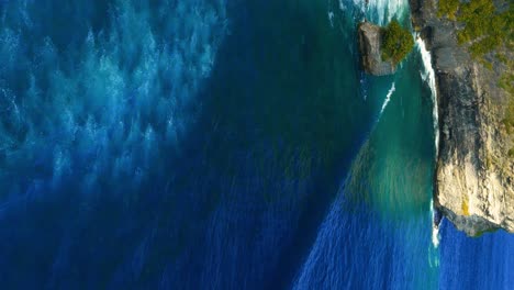 Vertical-Reveal-shot-of-the-Pura-Uluwatu-Temple-in-Bali,-with-the-green-cliffs-and-slow-rolling-swells-in-the-ocean