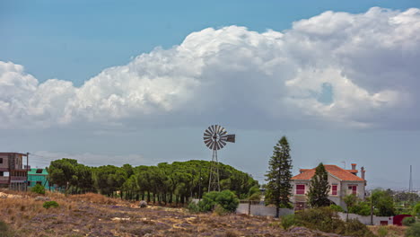 Timelapse-of-white-fluffy-clouds-blowing-over-windmill-and-tree-line-above-city