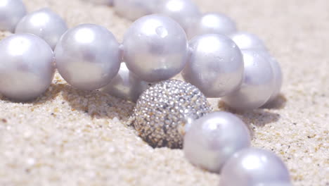 Cinematic-close-up-of-a-natural-pearl-necklace-with-silver-jewellery-laying-on-a-sandy-beach,-120-FPS,-Slomo