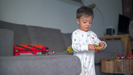 Slow-motion-of-a-young-toddler-wearing-pajamas-playing-with-a-yellow-car-toy-on-the-couch