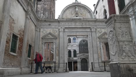 Old-Male-Walking-His-Dog-Through-The-Courtyard-Of-Scuola-Grande-di-San-Giovanni-Evangelista-In-Venice