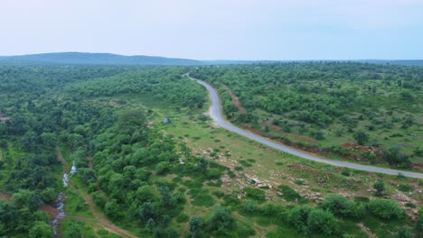 Vista-Aérea-De-Drones-De-Un-Camino-Forestal-A-Través-De-Una-Exuberante-Jungla-Verde-Con-Un-Telón-De-Fondo-Montañoso-En-Gwalior-Madhya-Pradesh-India