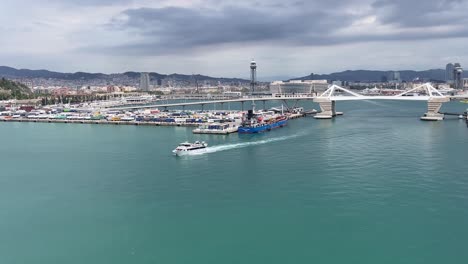 Scene-of-a-moving-ferry-boat-and-against-the-background-of-the-cityscape-view-of-the-Porta-d'Europa,-a-double-leaf-bascule-bridge-in-the-Port-of-Barcelona,-Spain