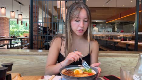 Young-happy-female-eating-a-ramen-noodle-in-an-upmarket-Japanese-restaurant-on-a-hot-sunny-day-in-england