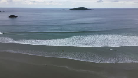 Lonely-Surfer-at-Cox-Bay-in-Tofino,-BC---Ocean-and-Beach-Aerial-View