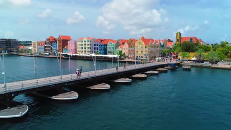 4K-Kino-Drohnenaufnahme-Der-Schwimmenden-Queen-Emma-Pontonbrücke-Mit-Farbenfrohen-UNESCO-Gebäuden-Im-Hintergrund-In-Willemstad,-Curaçao