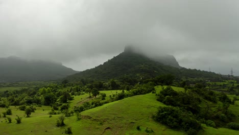 Aerial-drone-camera-moving-over-the-mountains-with-a-big-cloud-filled-with-water-flowing-over-the-mountains,-surrounded-by-greenery-and-a-spectacular-view-of-the-monsoon-season