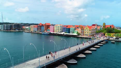 4K-Kino-Drohnenaufnahme-Der-Ikonischen-Schwimmenden-Queen-Emma-Pontonbrücke-Und-Der-Farbenfrohen-UNESCO-Gebäude-In-Willemstad,-Curaçao