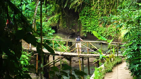 Tourists-going-on-wooden-bridge-to-see-Tibumana-waterfall-in-Bali,-handheld-view
