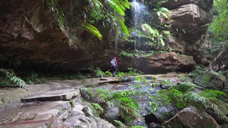 Indigenous-Australian-girl-walking-underneath-a-small-waterfall-in-the-Blue-Mountains,-NSW-Australia