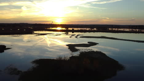 Sun-reflecting-on-watery-marshland-landscape,-aerial-drone-view