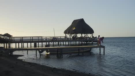 Kids-play-at-the-edge-of-a-pier-during-the-dusk-at-Punta-Gorda-beach-in-Roatan,-honduras---Handheld