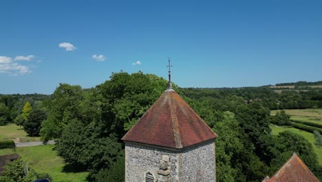 An-ascending-boom-shot-of-St-Lawrence-the-Martyr-church-in-Godmersham,-flying-above-the-church-tower-for-a-greater-view-of-the-fields-behind