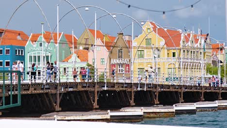 4k-60fps-cinematic-parallax-fly-by-pan-of-the-floating-Queen-Emma-Bridge-with-tourists-and-pedestrians-walking-over-it,-in-the-city-of-Willemstad,-Curacao
