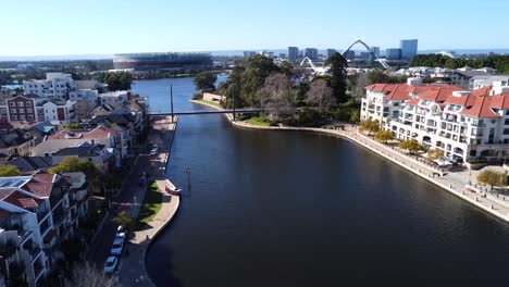 Drone-Aerial-View-travelling-backwards-over-Suspension-pedestrian-bridge-in-Claisebrook-Cove,-East-Perth-with-Optus-Stadium-and-Swan-River