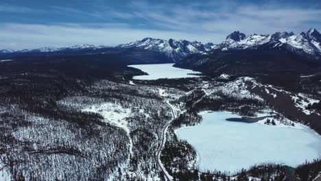 Panoramic-Aerial-View-Of-Frozen-Lakes-With-Forest-Mountains-During-Winter