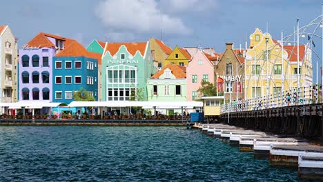 4k-24fps-pan-of-Queen-Emma-Bridge-opening-in-Willemstad,-featuring-the-iconic-colorful-World-Heritage-UNESCO-buildings-of-the-Handelskade-in-Punda,-Curacao