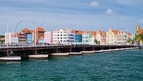 4k-60fps-cinematic-wide-parallax-fly-by-pan-of-the-floating-Queen-Emma-Bridge-with-tourists-and-pedestrians-walking-over-it,-in-the-city-of-Willemstad,-Curacao