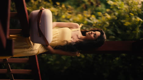 Beautiful-Young-Brunette-Woman-on-Balcony-in-Yellow-Dress,-Cooler-Box,-Cinematic-Warm-Natural-Lighting,-Forest-Background,-Slow-Motion-Establishing-Shot,-Vertical