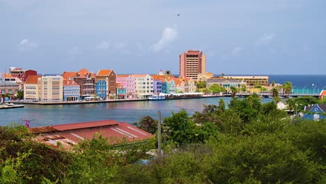 Slow-right-to-left-orbit-pan-of-Willemstad-city-featuring-the-iconic-colorful-world-heritage-UNESCO-buildings-of-the-Handelskade-in-Punda,-Curacao