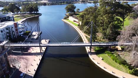 Drone-Aerial-View-over-people-walking-along-Suspension-pedestrian-bridge-in-Claisebrook-Cove,-East-Perth-and-Swan-River