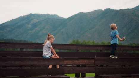 Boy-with-wild-flowers-looks-at-mountains-girl-sits-on-bench