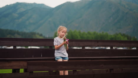 Little-girl-smells-small-bouquet-of-windflowers-on-bench