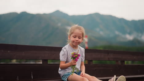 Blonde-child-holds-wild-flowers-sitting-on-wooden-bench