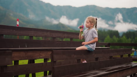 Little-girl-enjoys-wildflowers-aroma-sitting-on-wooden-bench