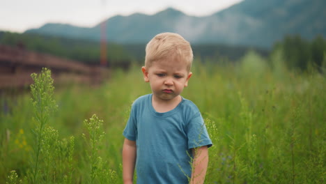 Unhappy-little-boy-grimaces-walking-along-meadow-grass