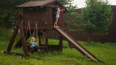 Little-girl-points-ahead-on-slide-and-brother-plays-swings