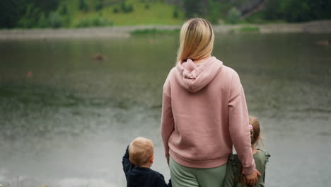 Mother-and-little-children-enjoy-calm-lake-standing-on-bank