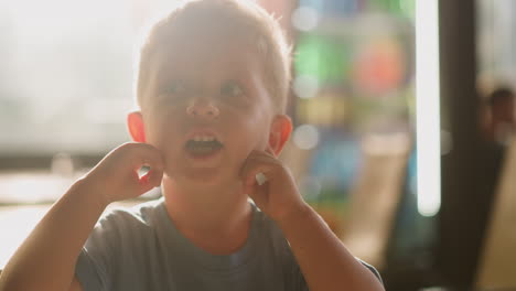 Little-boy-with-open-mouth-closes-ears-by-fingers-in-room