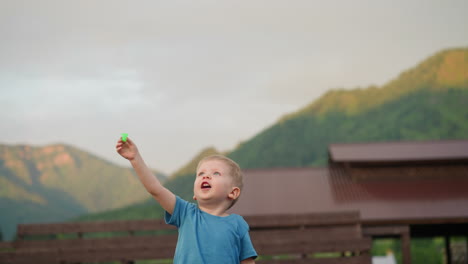 Excited-boy-launches-flying-toy-on-ground-against-mountains
