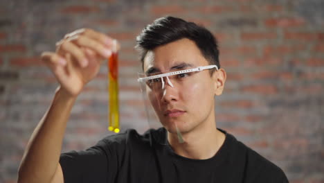Asian-medical-student-looks-at-test-tube-with-liquid-in-lab