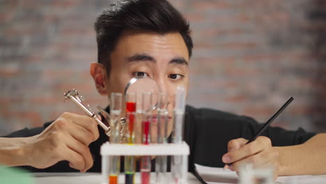 Asian-chemist-looks-at-test-tubes-through-magnifying-glass