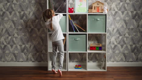 Little-girl-in-pajamas-takes-toys-off-box-on-rack-at-home