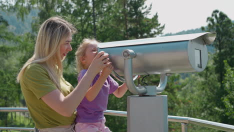 Mother-helps-girl-look-through-binoculars-at-resort-deck
