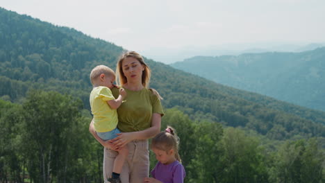 Tired-woman-with-little-children-stand-against-green-hills