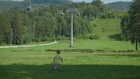 Little-boy-walks-along-meadow-under-contemporary-ropeway