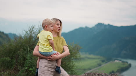 Happy-woman-with-little-son-enjoys-view-near-mountains
