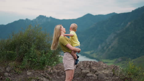 Young-mother-adjusts-loose-hair-holding-toddler-boy-on-hill