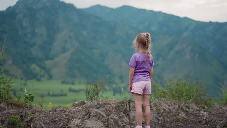 Little-girl-with-plait-enjoys-view-of-large-mountains
