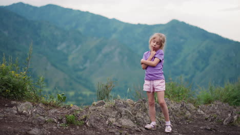 Funny-little-child-touches-cheek-with-finger-on-rocky-hill